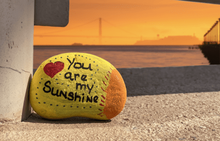 A painted rock which reads "You are my sunshine" placed near a beach pier