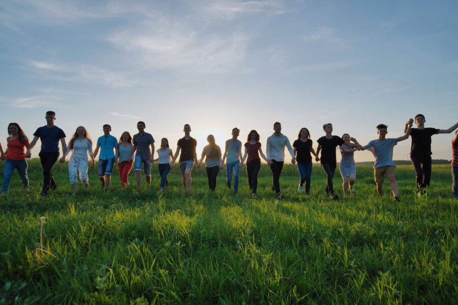 A large group of teenagers holding hands walking across a field
