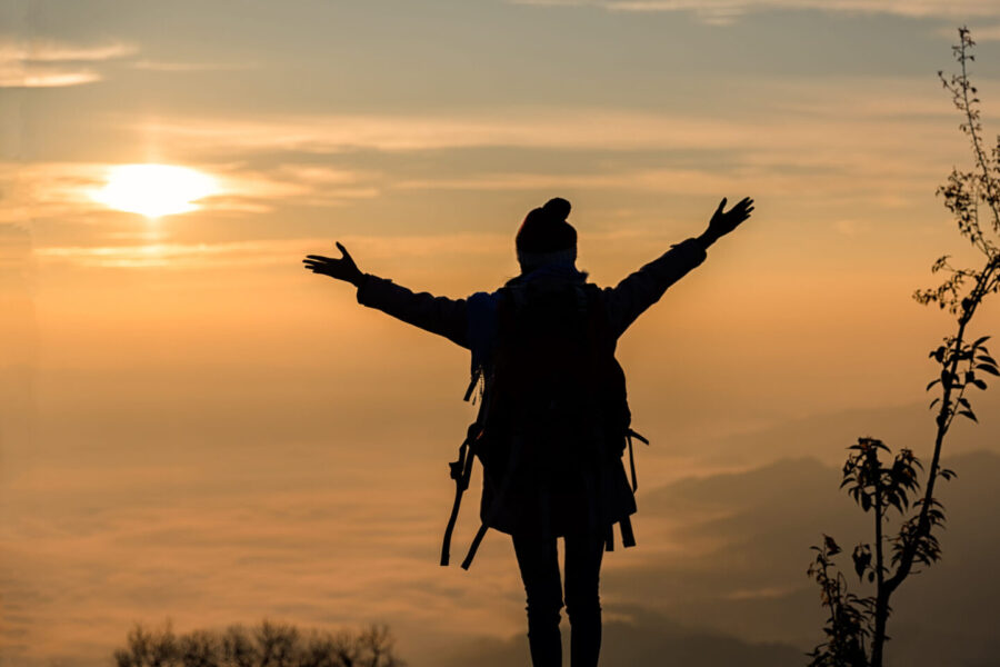 A teen girl with upraised arms on a mountaintop at sunset