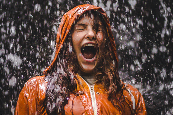 A teenage girl laughing in joy as she stands in the pouring rain