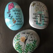Painted rocks with encouraging messages like "Believe there are better days ahead" and "One day at a time" and "Every day is a new beginning. Take a deep breath and start again."