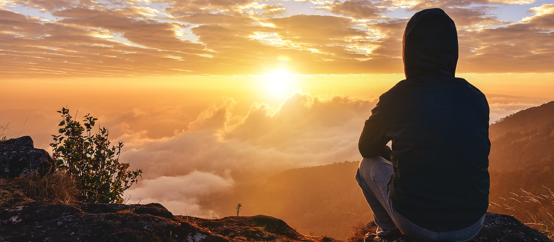 A student sitting alone on a mountaintop contemplating a beautiful sunset