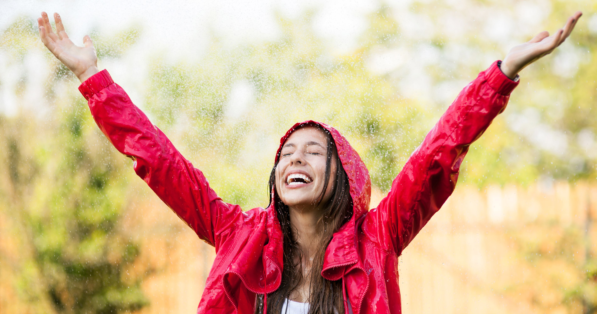 A laughing teenage girl raising her arms in joy as the rain falls on her face