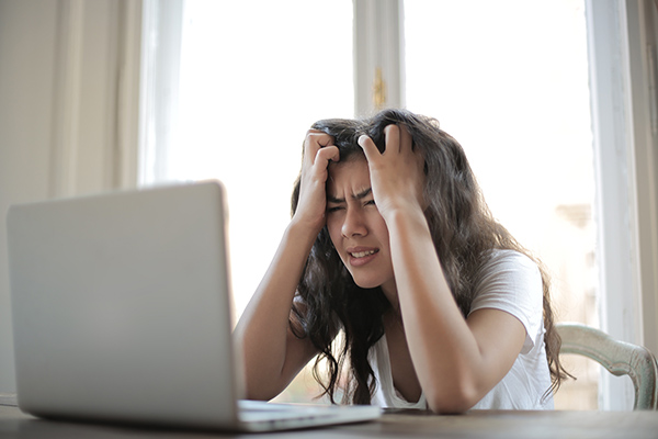 A frustrated or stressed teenage student in front of a computer with her hands on her head