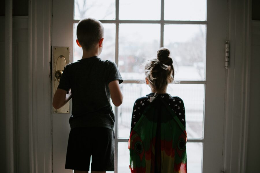 two children stuck indoors looking out the window