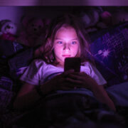 A tween girl up late at night, her face lit by the glow of her smartphone