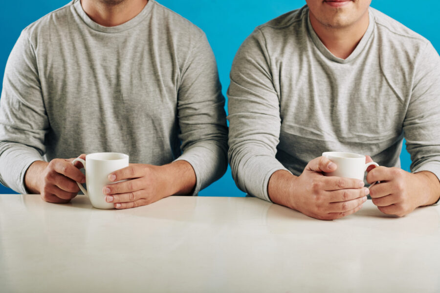 Unrecognizable male twins wearing same clothes sitting at table