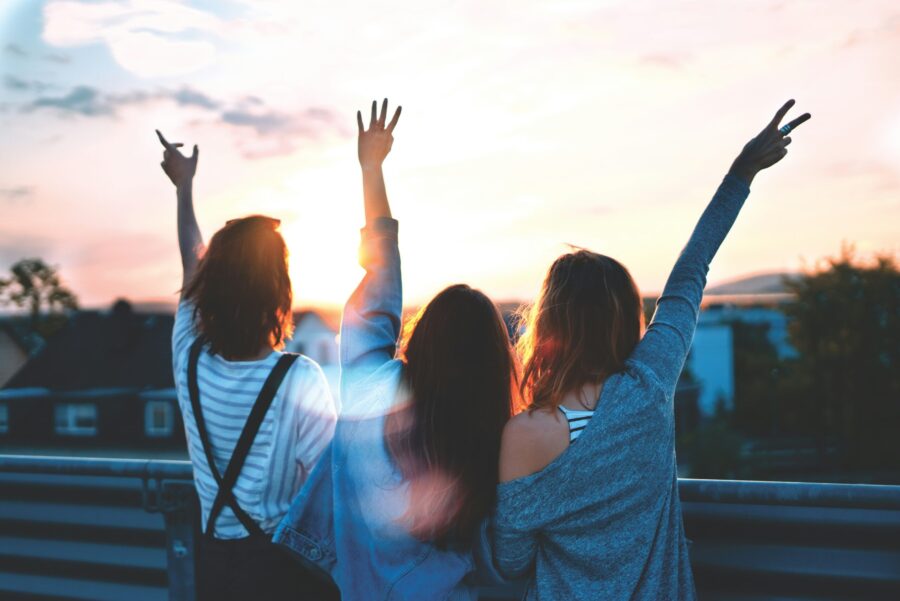 Three teen girls waving hands in the air at sunset